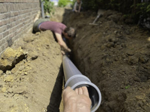 A man carries a sewer pipe and places it in the dirt foundation laid out for it.