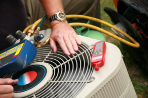 A worker uses several tools to help fix a broken AC unit.