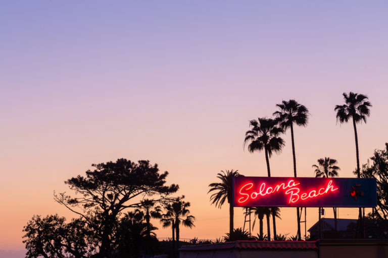 A view of palm trees and a sign for the town of Solana Beach, CA