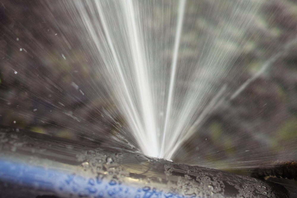 A closeup of a metal pipe bursting and leaking water