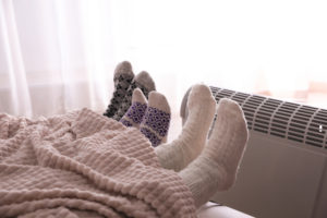 Several people under a blanket wearing wool socks in front of an electric heater