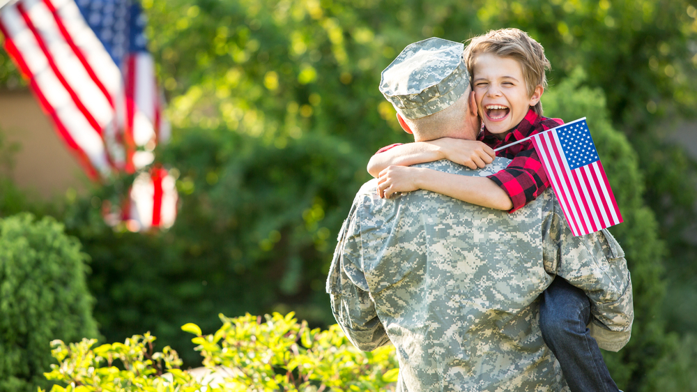 A soldier picks up a happy child holding an American flag